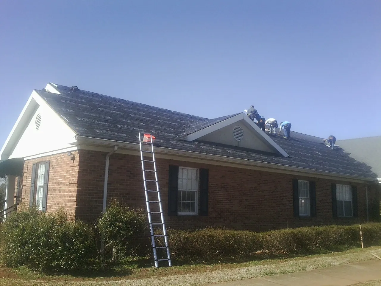 Crew tearing shingles off a brick ranch roof with a ladder set — Metal Roof Repair work by our crew in Cerro Gordo