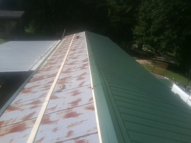 Old rusted panels beside newly installed green metal roofing — Wind Damage Roof Repair by Roofing Brothers in Cerro Gordo