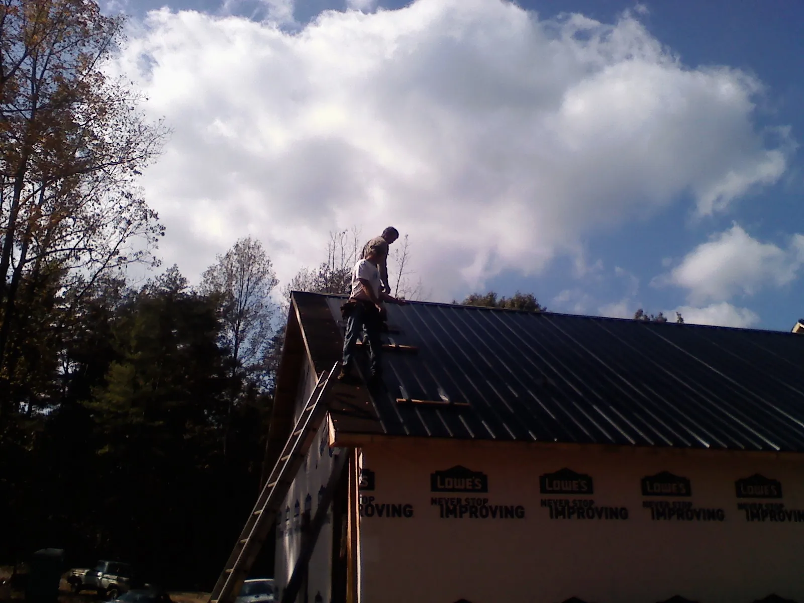 Roofer fastening dark metal panels high against a cloudy sky, from a Roof Inspection job in Cerro Gordo