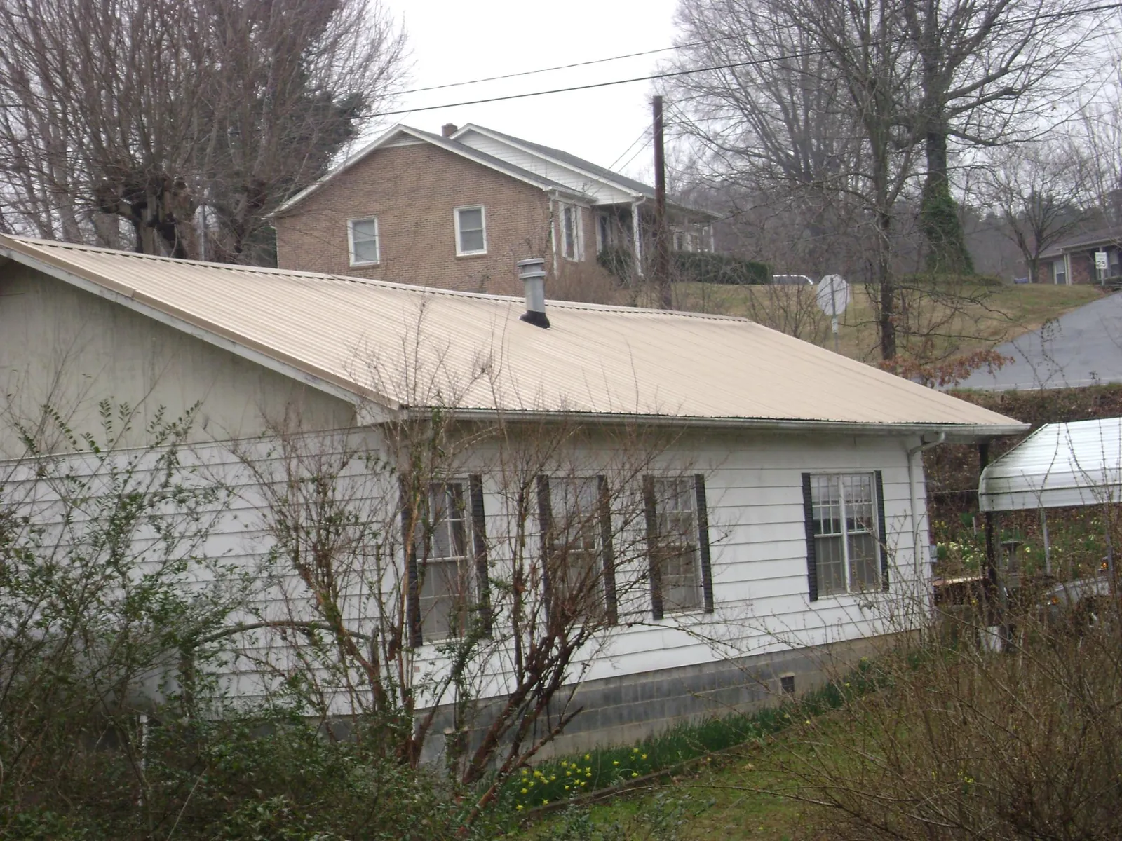 Tan metal roof on a white sided house set into a hillside — Commercial Roofing by Roofing Brothers in Cerro Gordo